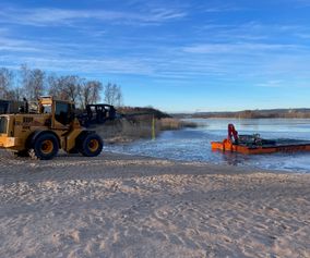 Barge launched and assisted by a wheel loader in shallow water.